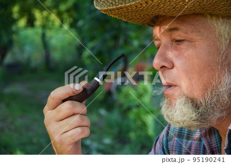 Senior adult man with white beard smoking tobacco pipe outdoors 95190241
