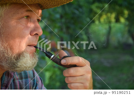 Senior adult man with white beard smoking tobacco pipe outdoors 95190251