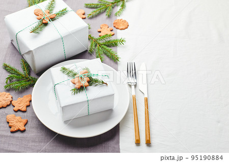 Christmas festive table setting, plate with gift decorated with spruce sprigs and gingerbread Christmas festive table setting, plate with gift decorated with spruce sprigs and gingerbread 95190884