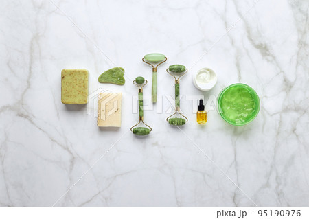 Cosmetic skin care products, jade stone face massager, creams, gel and oil. Roller massage of the face. Flat lay, top view 95190976