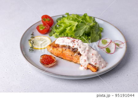 Salmon (trout) with creamy Champagne sauce with red caviar, arugula, cherry tomatoes, radish and lemon. Traditional French dish. Selective focus, close-up. 95191044