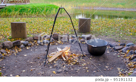 Cooking in a pot on an open fire in nature. Bowler on a bonfire in the forest. Cast iron cauldron on the fire on the background of the pond. 95191132