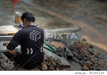 Utility worker using tool to fixing broken water main for commercial building water supplies during a rain. Utility worker using tool to fixing broken water main for commercial building water supplies during a rain. 95191154