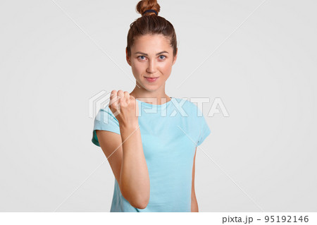 Serious strict Caucasian young woman shows fist at camera, warns you about punishment, shows her power, dressed in casual clothes, stands against white background. Dont make fun with me, please! 95192146
