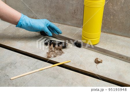 Woman removing hair clump from the shower drain. 95193948