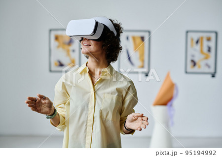 Young girl standing and gesturing in virtual reality glasses visiting virtual art gallery Young girl standing and gesturing in virtual reality glasses visiting virtual art gallery 95194992