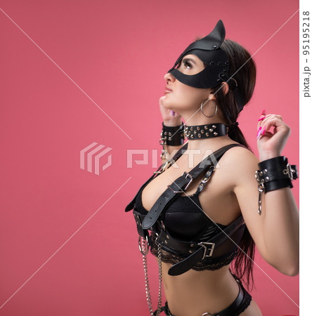 brunette in bdsm leather straps on a pink background in a cat mask in handcuffs for sex games brunette in bdsm leather straps on a pink background in a cat mask in handcuffs for sex games 95195218