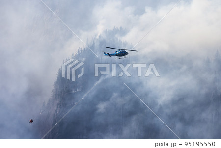Wildfire Service Helicopter flying over BC Forest Fire and Smoke on the mountain near Hope 95195550