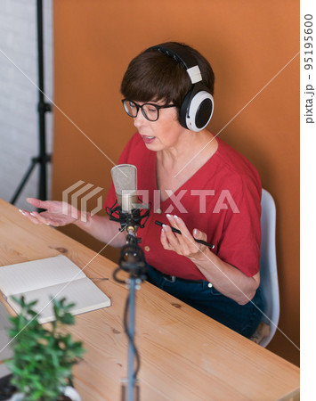 Woman making podcast recording for her online show. Attractive business woman using headphones front of microphone for a radio broadcast 95195600