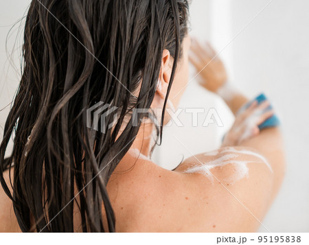 Naked woman with takes a shower. Woman washes her arms with shower gel and blue washcloth. Morning routine in urban apartment. 95195838