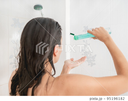 Naked woman with short hair takes a shower. Woman squeezes shampoo out of plastic bottle. Usual routine in white bathroom. Naked woman with short hair takes a shower. Woman squeezes shampoo out of plastic bottle. Usual routine in white bathroom. 95196182