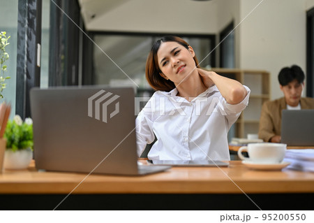 Exhausted and overworked Asian businesswoman suffering from neck pain at her desk. Exhausted and overworked Asian businesswoman suffering from neck pain at her desk. 95200550