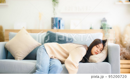 Asian woman resting at home on couch, feeling exhausted after work 95200720