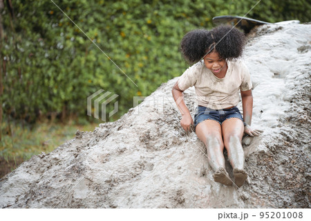 Happy African-American child girl playing on heap of wet soil during raining in rainy season. Happy African-American child girl playing on heap of wet soil during raining in rainy season. 95201008