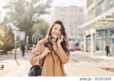 Lifestyle portrait happy Asian kazakh woman talking on mobile phone and laughing Lifestyle portrait happy Asian kazakh woman talking on mobile phone and laughing 95201304