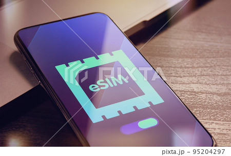 eSIM - Embedded SIM technology concept with smartphone very close lying on a wooden table with esim icon on the screen 95204297