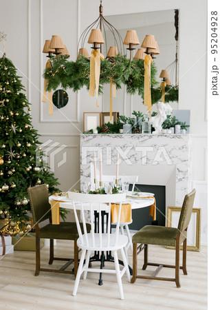 Stylish festive Christmas table with vintage chairs near the marble fireplace and Christmas tree in the living room or dining room in the house Stylish festive Christmas table with vintage chairs near the marble fireplace and Christmas tree in the living room or dining room in the house 95204928