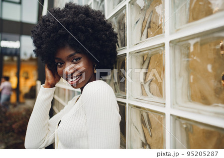 African young woman looking happy while posing against glass wall 95205287