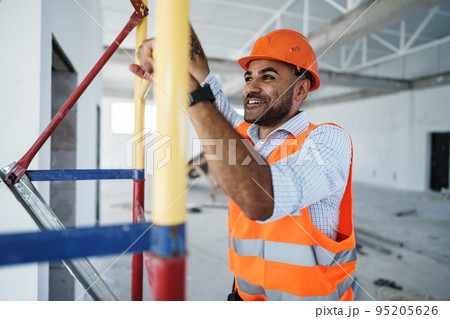 Young handsome builder climbing on scaffolding at construction site 95205626
