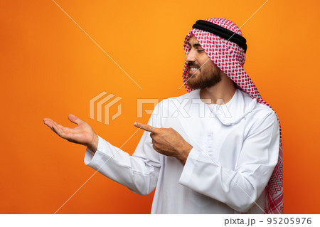 Young Arab man pointing hand to copy space on orange background Young Arab man pointing hand to copy space on orange background 95205976