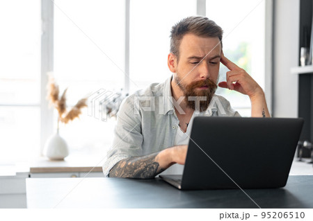 Stylish bearded man working on laptop from home sitting at the table 95206510