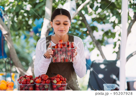Young positive saleswoman at work, holding strawberries in her hands 95207928