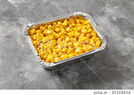 Aluminium foil container with yellow boiled corn kernels on gray stone tabletop 95208836