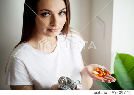 Woman with white measuring tape and many slim pills in her hand Woman with white measuring tape and many slim pills in her hand 95209770