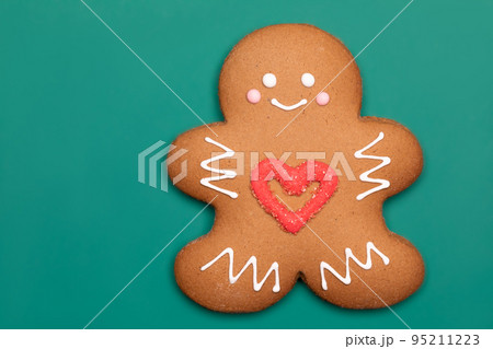 Christmas Gingerbread man biscuit with red heart icing on green background 95211223