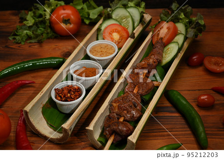 Grilled meat in bamboo barrel plat served with Sichuan pepper, mala powder, Chinese spices and vegetable on rustic wooden table 95212203