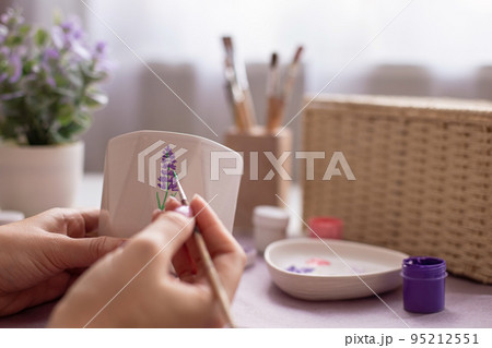 Female paints with a brush a sprig of a lavender flower, on a white ceramic pot 95212551