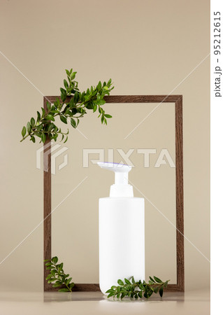 White cosmetic bottle , stands in an empty wooden frame with branches of a green plant White cosmetic bottle , stands in an empty wooden frame with branches of a green plant 95212615