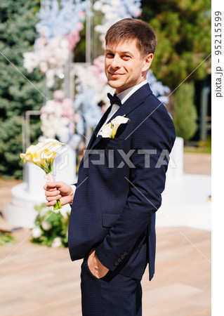 the groom is in a dark blue suit with a boutonniere and a bouquet of callas. the groom is in a dark blue suit with a boutonniere and a bouquet of callas. 95215599