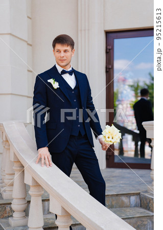 the groom is in a dark blue suit with a boutonniere and a bouquet of callas. 95215613