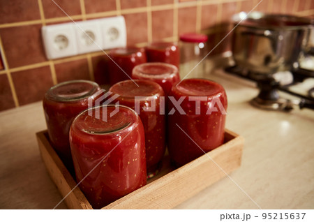 Still life with sterilized tins of freshly brewed tomato sauce, passata or juice, upside down on a wooden crate. Canning organic homegrown vegetables for the winter. Making preserves. Conservation 95215637