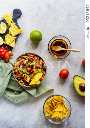Traditional Mexican vegetable salad - cowboy caviar in bowl with ingredients and nachos on concrete background  95215640