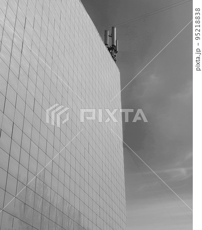 Black-and-white photo The exterior wall of a modern commercial-style building, paneled with tiles, on the roof modern antennas against the sky Black-and-white photo The exterior wall of a modern commercial-style building, paneled with tiles, on the roof modern antennas against the sky 95218838