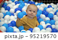 One year old boy sits in a pool with colorful plastic balls and plays with them 95219570