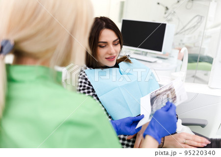 Dental clinic doctor shows a panoramic x-ray picture to his patient. Doctor explains to her patient the condition of her teeth Dental clinic doctor shows a panoramic x-ray picture to his patient. Doctor explains to her patient the condition of her teeth 95220340