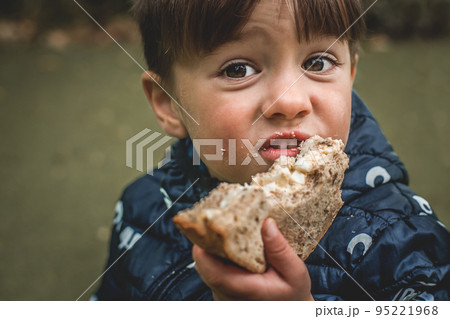 Upset poor hungry kid is eating bread. Homeless with dirty face. Portrait of child boy with big eyes. Crisis, peace, stop aggression, War in Ukraine. Sad refugee. Face asking for food 95221968