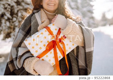 Pretty Woman holding a giftbox with red ribbon in the winter park. Happy winter time. New year's. 95222868