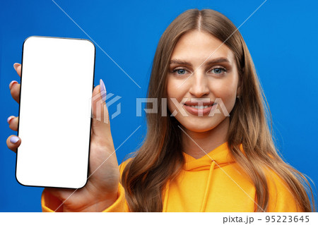 Young woman showing big blank cellphone screen on blue background in studio 95223645