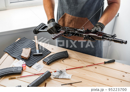 Close up of young man in apron disassembling a gun above the table 95223700