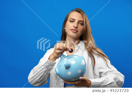 Young caucasian woman holding a piggy bank.against blue background Young caucasian woman holding a piggy bank.against blue background 95223720