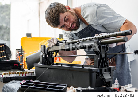 The gunsmith maintaining his rifle in a workshop The gunsmith maintaining his rifle in a workshop 95223782