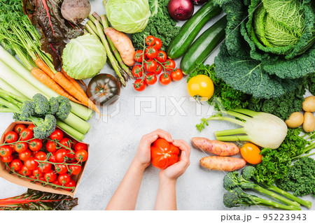 Healthy eating concept. Child's hands holding tomato. Organic vegetables broccoli cauliflower carrots kale pak choy onions. Healthy local farm produce on white wooden table, top view, selective focus Healthy eating concept. Child's hands holding tomato. Organic vegetables broccoli cauliflower carrots kale pak choy onions. Healthy local farm produce on white wooden table, top view, selective focus 95223943