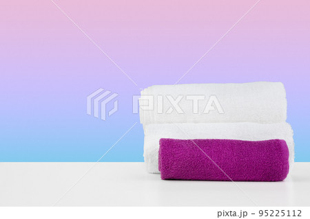Stacked clean towels on white table against color background 95225112