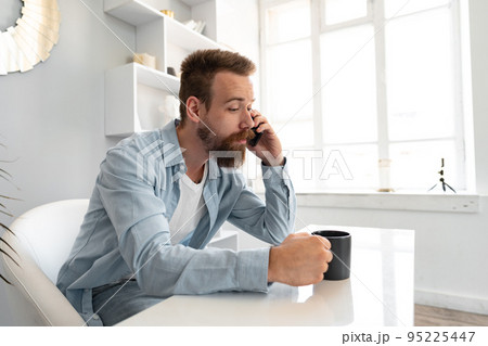 Young bearded businessman working from home sitting at the desk and talking on mobile phone 95225447