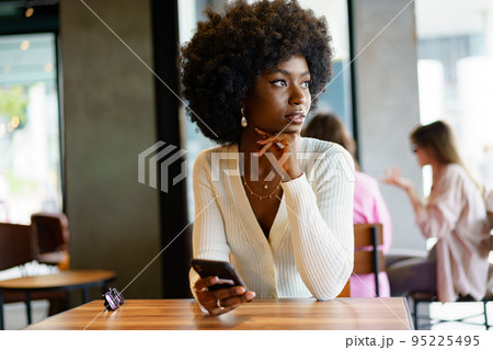 Young afro woman using mobile phone at coffee shop Young afro woman using mobile phone at coffee shop 95225495