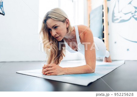 Middle-aged woman stretching on exercise mat at a gym. 95225628